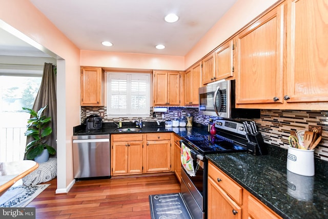 kitchen featuring sink, light wood-type flooring, dark stone counters, stainless steel appliances, and backsplash