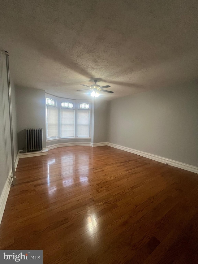 empty room with ceiling fan, dark hardwood / wood-style floors, radiator, and a textured ceiling