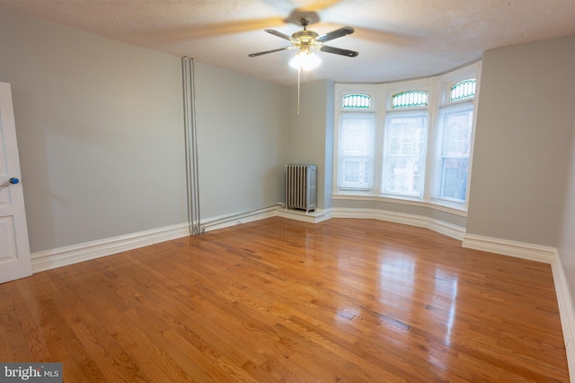 empty room with ceiling fan, radiator, a textured ceiling, and light hardwood / wood-style flooring