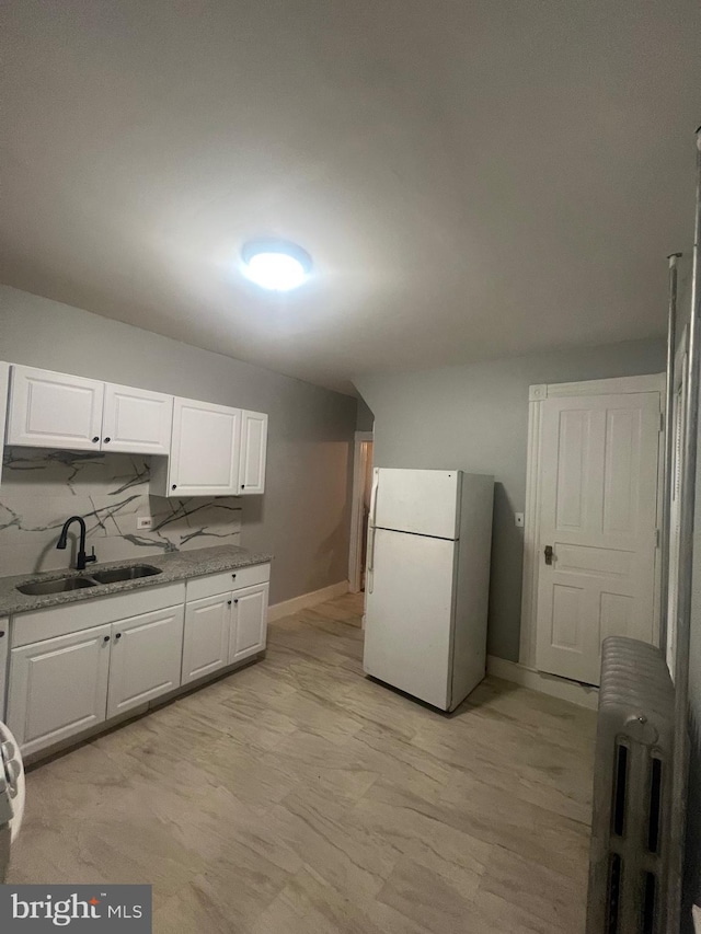 kitchen with light stone countertops, white cabinetry, white fridge, and sink