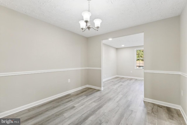 spare room with an inviting chandelier, a textured ceiling, and light hardwood / wood-style floors