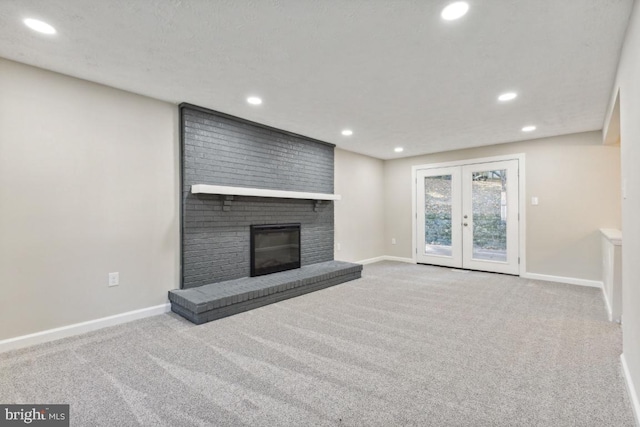 unfurnished living room with a brick fireplace, light carpet, and french doors