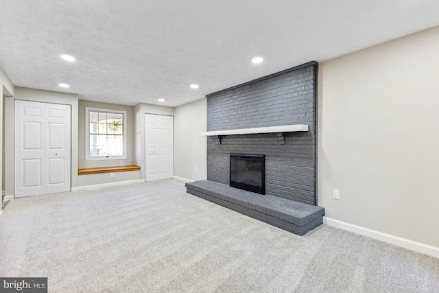 unfurnished living room featuring a brick fireplace, light colored carpet, and a textured ceiling