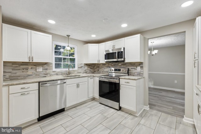 kitchen featuring white cabinetry, stainless steel appliances, decorative light fixtures, and sink