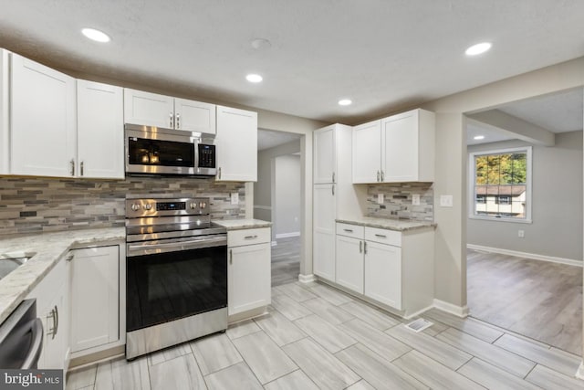 kitchen with white cabinetry, appliances with stainless steel finishes, light stone counters, and decorative backsplash