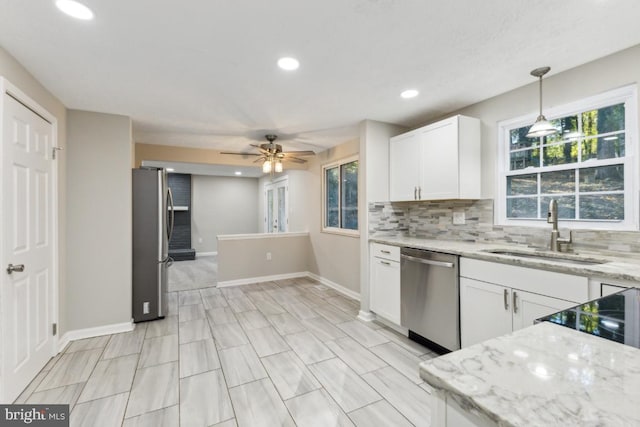 kitchen with sink, appliances with stainless steel finishes, hanging light fixtures, light stone counters, and white cabinets