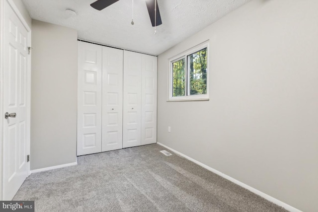 unfurnished bedroom featuring ceiling fan, a closet, light carpet, and a textured ceiling