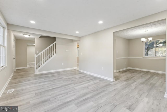 unfurnished living room featuring a notable chandelier and light wood-type flooring