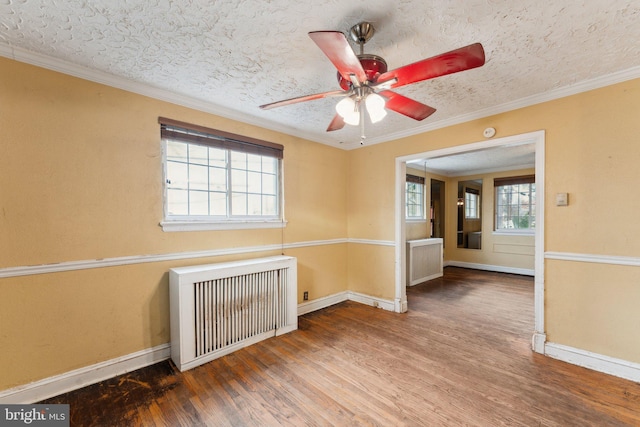 empty room featuring hardwood / wood-style flooring, ornamental molding, radiator, and a textured ceiling