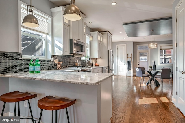 kitchen with hanging light fixtures, appliances with stainless steel finishes, white cabinets, and a kitchen breakfast bar