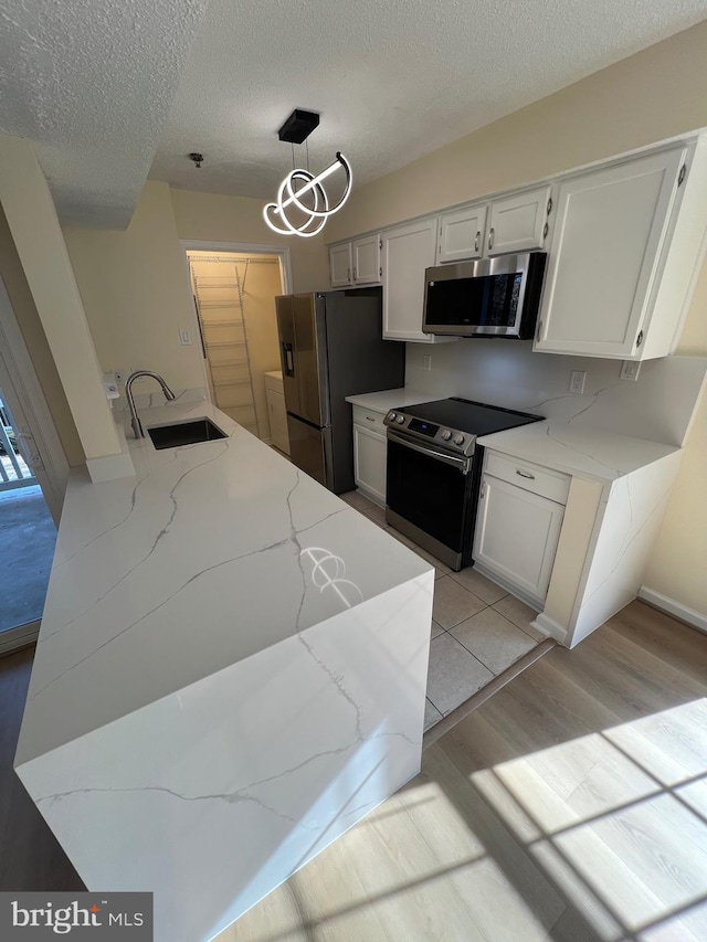 kitchen featuring sink, white cabinetry, light stone counters, decorative light fixtures, and appliances with stainless steel finishes