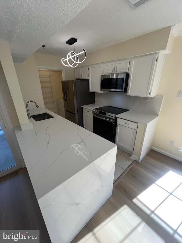 kitchen with appliances with stainless steel finishes, decorative light fixtures, sink, white cabinets, and a textured ceiling