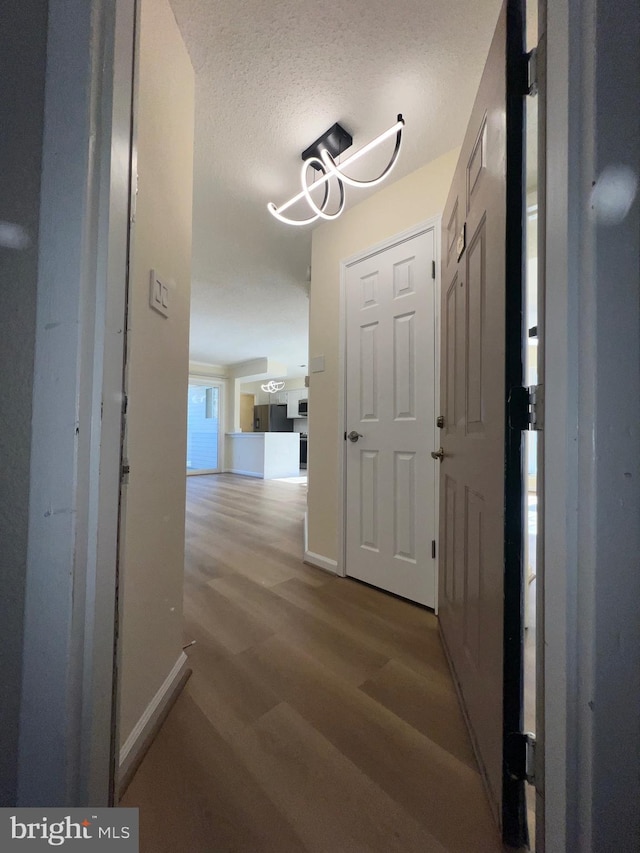 hall featuring a notable chandelier, a textured ceiling, and light hardwood / wood-style flooring