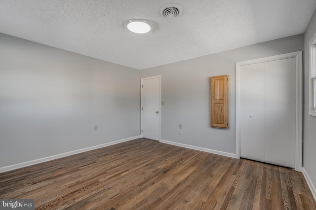 unfurnished bedroom featuring a textured ceiling, dark hardwood / wood-style flooring, and a closet