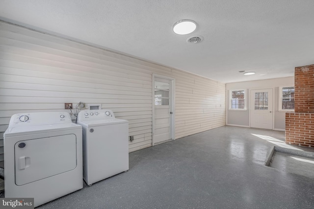 laundry room with washing machine and dryer, a textured ceiling, and wood walls