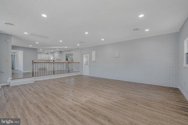 unfurnished room featuring brick wall, light wood-type flooring, and a textured ceiling