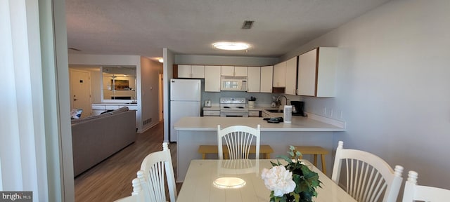 kitchen featuring sink, a textured ceiling, light wood-type flooring, kitchen peninsula, and white appliances