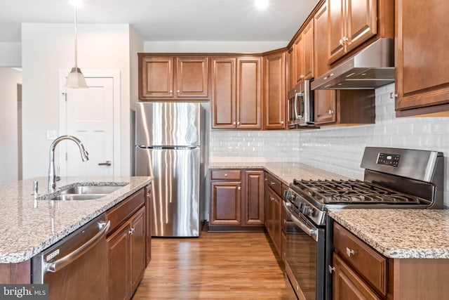 kitchen with appliances with stainless steel finishes, pendant lighting, sink, light stone counters, and light hardwood / wood-style floors