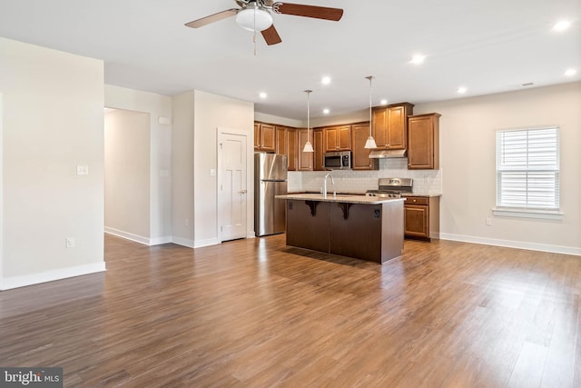 kitchen with a breakfast bar, hardwood / wood-style flooring, appliances with stainless steel finishes, pendant lighting, and a kitchen island with sink