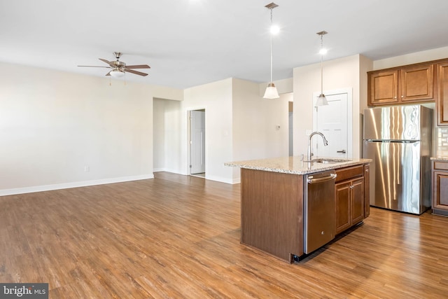 kitchen featuring decorative light fixtures, an island with sink, sink, stainless steel appliances, and light stone countertops