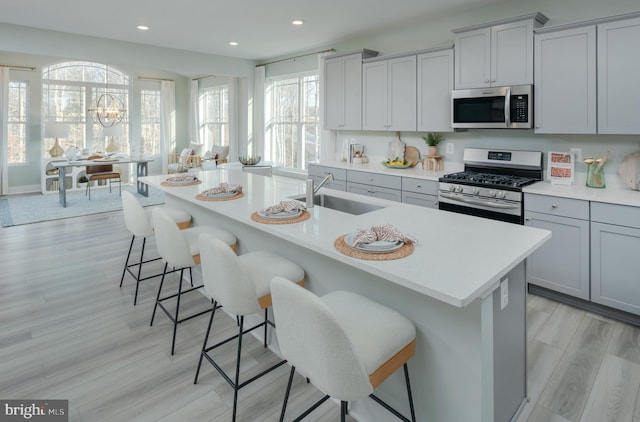 kitchen with a breakfast bar, sink, appliances with stainless steel finishes, an island with sink, and light hardwood / wood-style floors