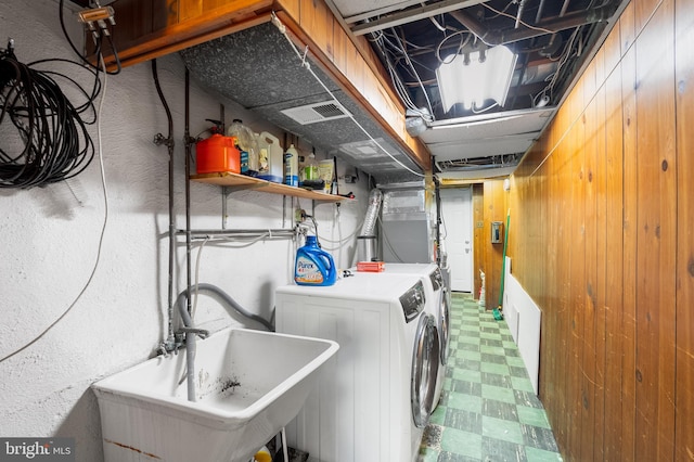 laundry area featuring washing machine and clothes dryer, wooden walls, and sink