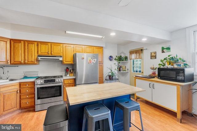 kitchen with a kitchen island, appliances with stainless steel finishes, butcher block counters, a kitchen bar, and light wood-type flooring