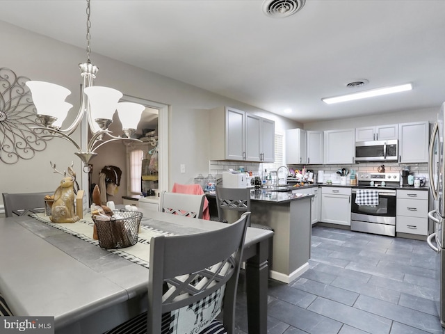 kitchen with decorative light fixtures, tasteful backsplash, white cabinetry, sink, and stainless steel appliances