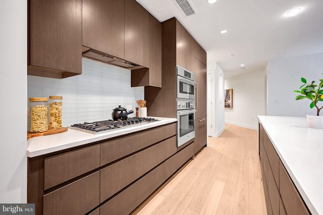 kitchen featuring backsplash, light hardwood / wood-style floors, premium range hood, and appliances with stainless steel finishes