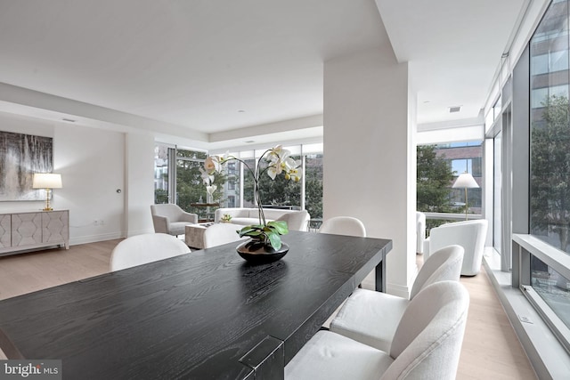 dining space with light hardwood / wood-style flooring, a healthy amount of sunlight, and a wall of windows