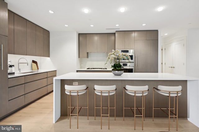 kitchen featuring sink, a breakfast bar area, light wood-type flooring, gas cooktop, and backsplash