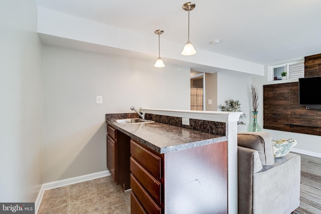 kitchen with a peninsula, a sink, baseboards, dark countertops, and decorative light fixtures