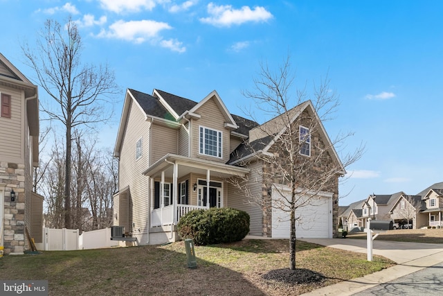 traditional home featuring a garage, concrete driveway, covered porch, fence, and a front lawn