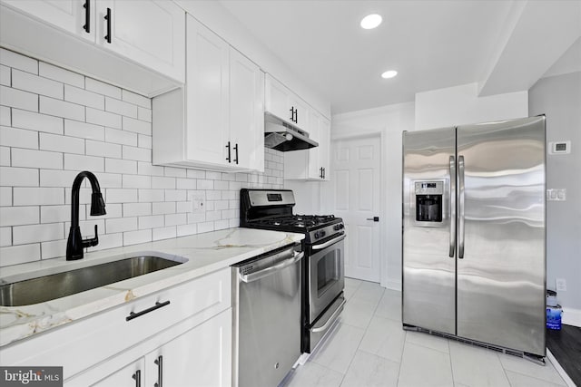 kitchen with sink, appliances with stainless steel finishes, white cabinetry, light stone countertops, and decorative backsplash