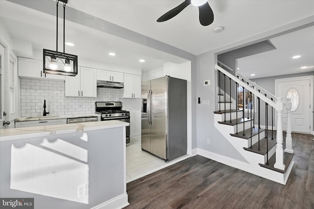 kitchen with appliances with stainless steel finishes, white cabinetry, sink, backsplash, and hanging light fixtures