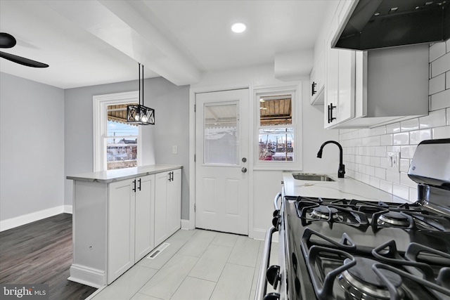 kitchen with sink, hanging light fixtures, light stone countertops, gas stove, and white cabinets