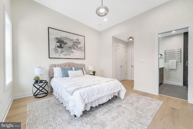 bedroom featuring a closet, wood-type flooring, ensuite bathroom, and vaulted ceiling