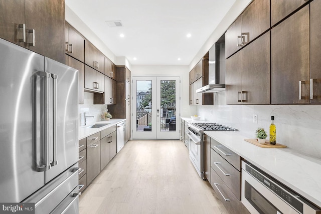 kitchen with wall chimney range hood, sink, high end appliances, tasteful backsplash, and french doors