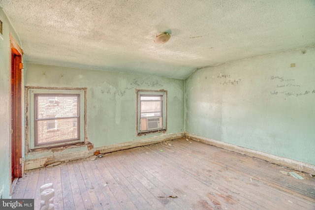 empty room featuring cooling unit, vaulted ceiling, a textured ceiling, and light wood-type flooring