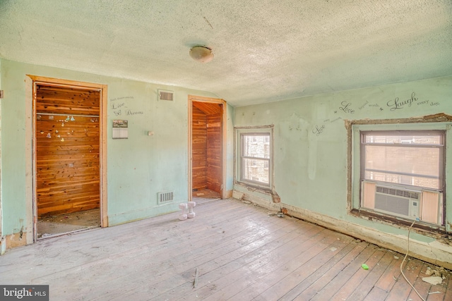 empty room with cooling unit, a textured ceiling, and light wood-type flooring