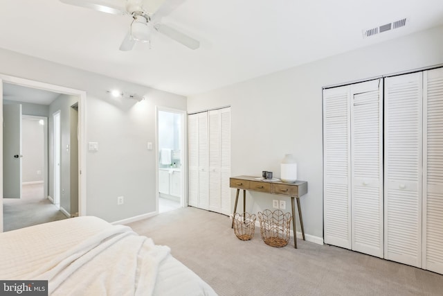 bedroom featuring ceiling fan, light colored carpet, and two closets