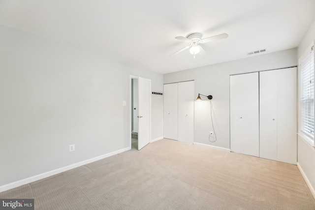 unfurnished bedroom with multiple windows, light carpet, two closets, and ceiling fan