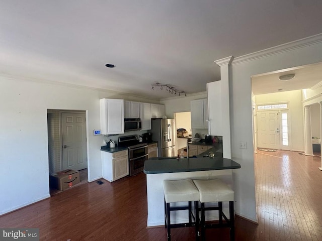 kitchen featuring white cabinetry, ornamental molding, appliances with stainless steel finishes, dark hardwood / wood-style floors, and kitchen peninsula