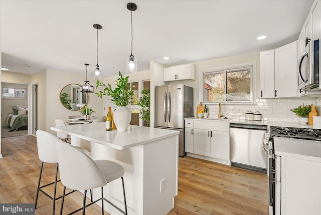 kitchen featuring appliances with stainless steel finishes, pendant lighting, white cabinetry, sink, and a center island