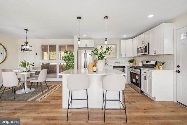 kitchen with appliances with stainless steel finishes, pendant lighting, white cabinets, and light hardwood / wood-style flooring