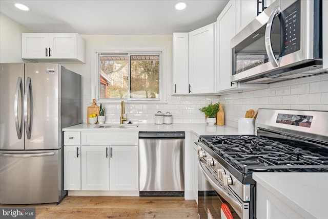 kitchen featuring stainless steel appliances, sink, white cabinets, and light wood-type flooring