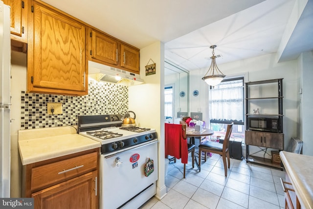 kitchen with white gas range, light tile patterned floors, hanging light fixtures, and backsplash