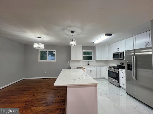 kitchen with sink, white cabinetry, stainless steel appliances, a kitchen island, and decorative light fixtures