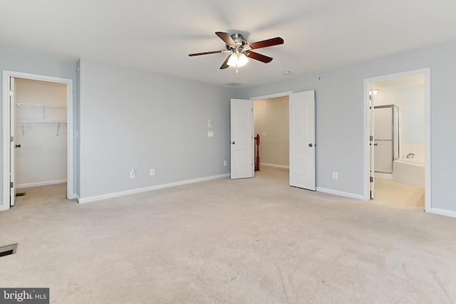 unfurnished bedroom featuring connected bathroom, a walk in closet, light carpet, a closet, and ceiling fan