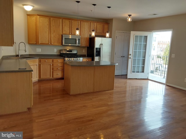 kitchen featuring sink, a center island, hanging light fixtures, appliances with stainless steel finishes, and light hardwood / wood-style floors